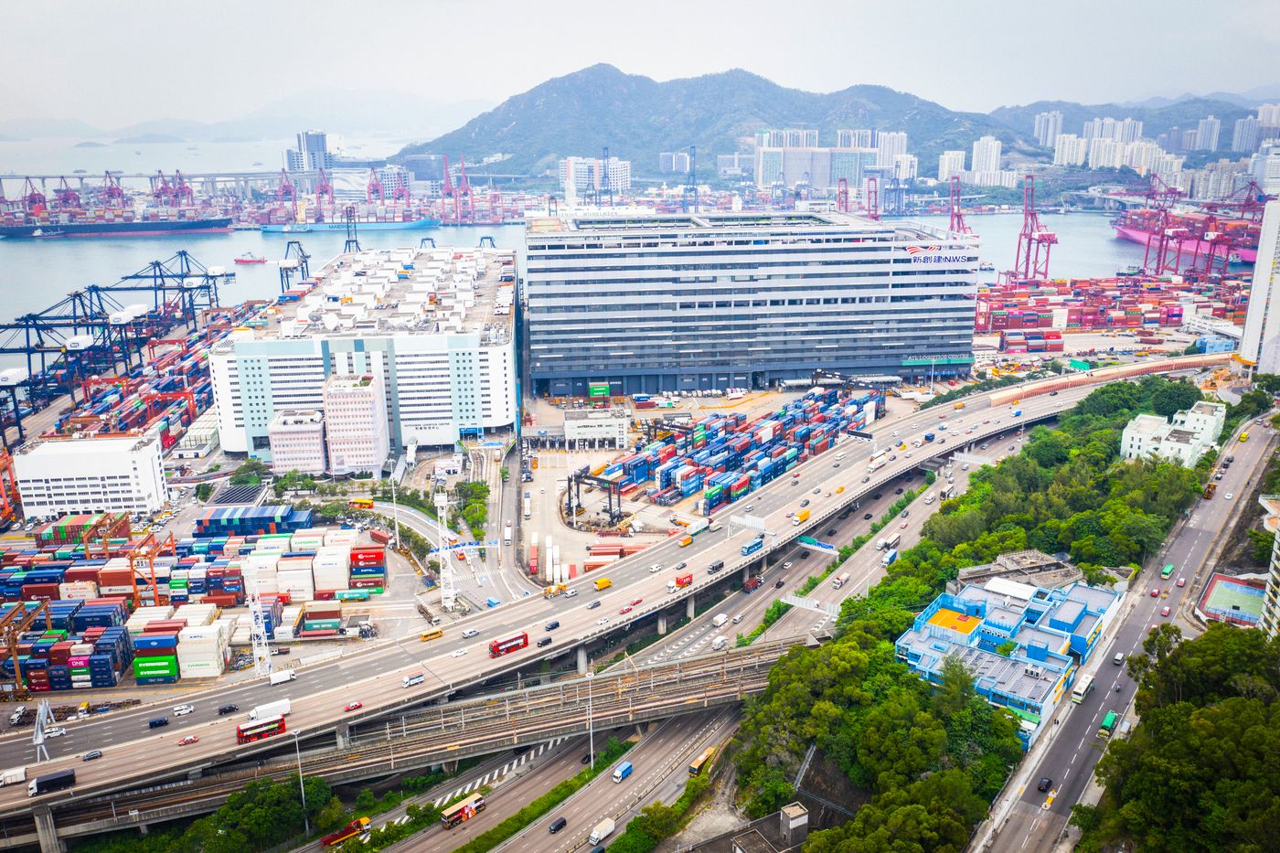 A container terminal seen from above: ships at the quay, stacked containers, and the roads and railway that carry them inland.